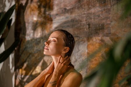 Portrait of young woman standing with eyes closed and washing her body while taking shower