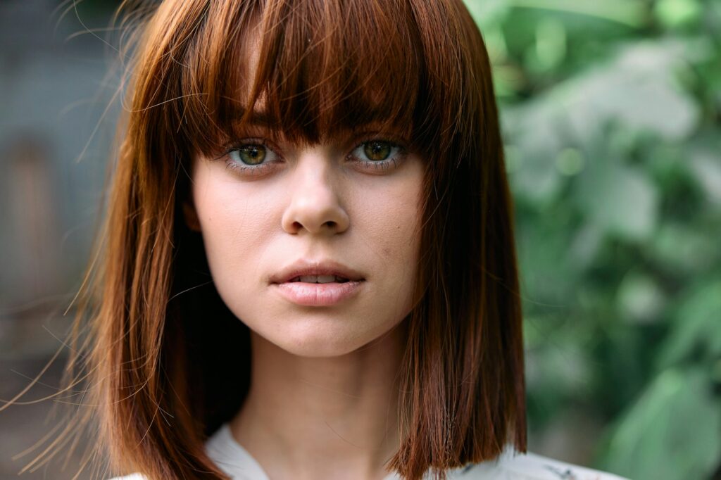 Young woman with bangs in white shirt surrounded by lush green plants in closeup view